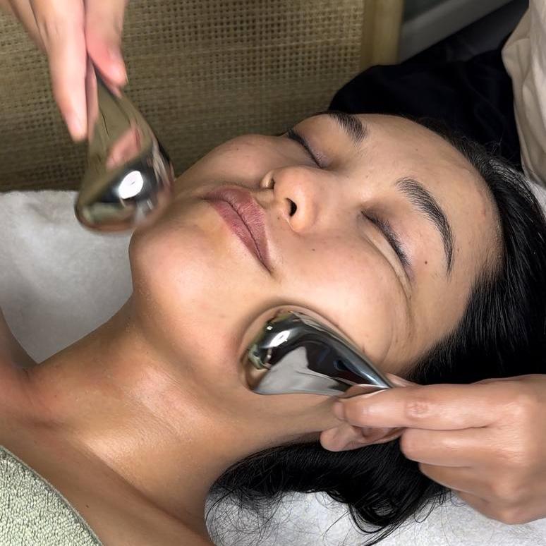 A person receiving a cryotherapy treatment on their face, with a hand holding a metal cryo device against their skin.