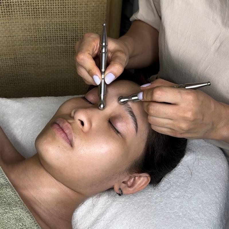 A close-up image of a facial pen being used by a professional on a client's face, with the client lying down and the professional using the pen to manipulate the facial muscles.